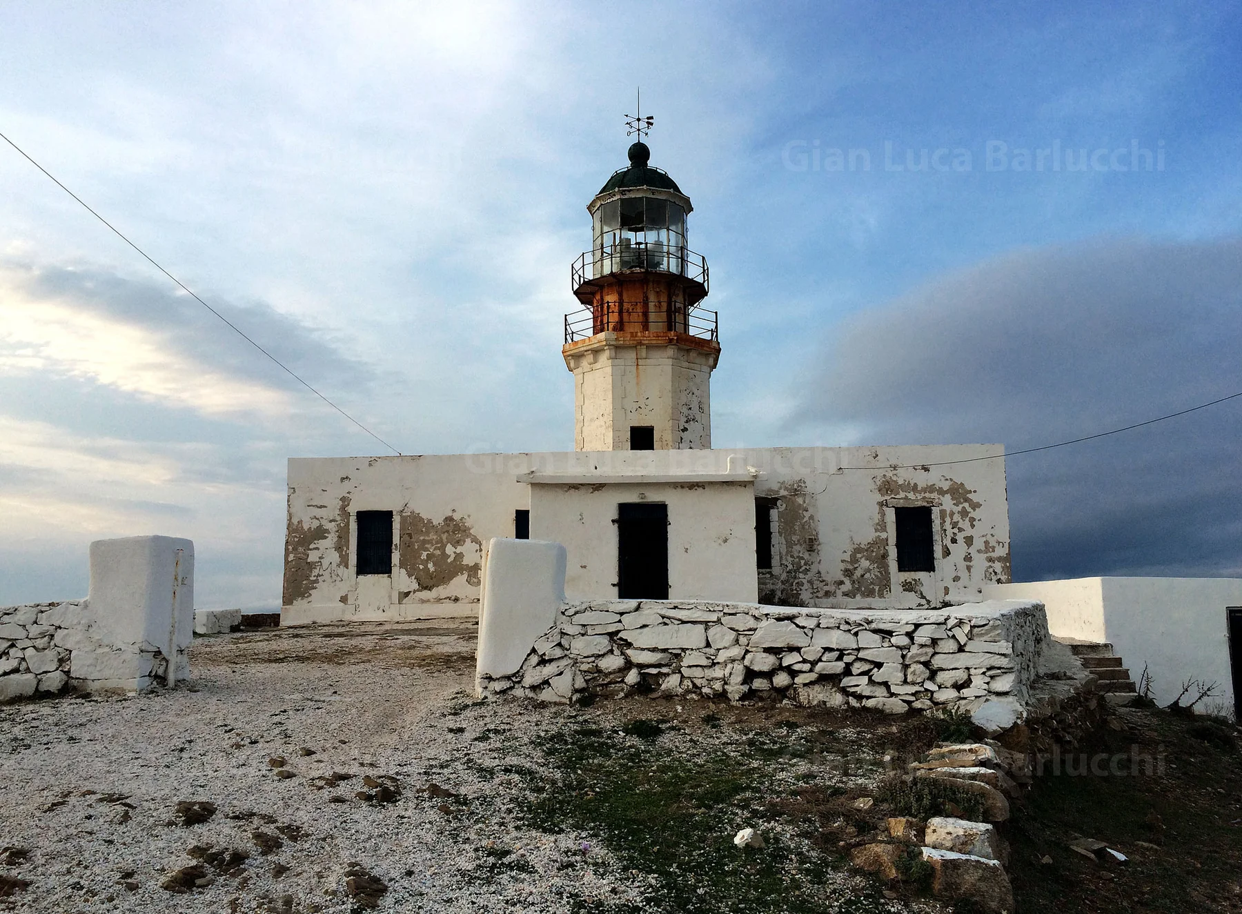 Weathered lighthouse above a white building and stone walls on Mykonos