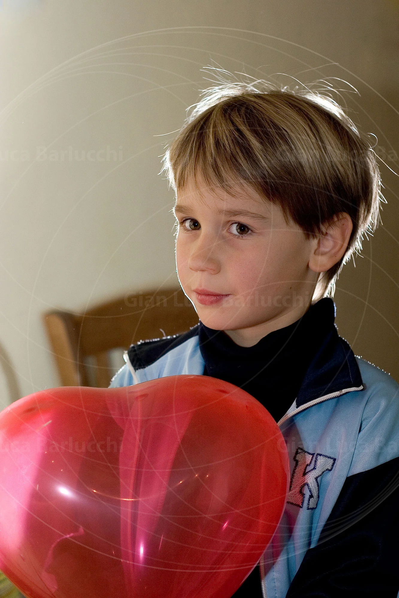 Child holding a red balloon while seated indoors