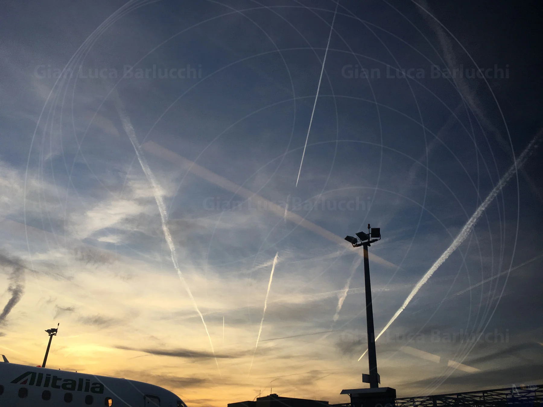 Aircraft trails crisscrossing the sky above an airport at sunset