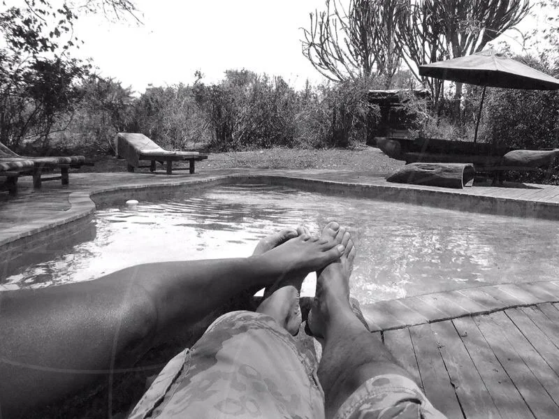 Black-and-white view of a person’s outstretched legs beside a swimming pool