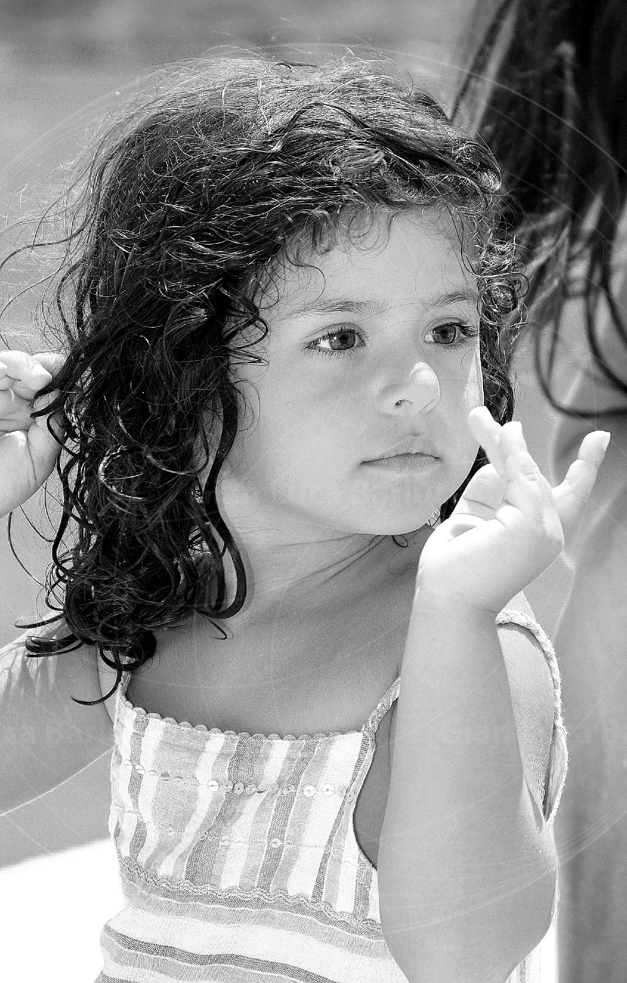 Black-and-white portrait of a curly-haired child with a hand near their face
