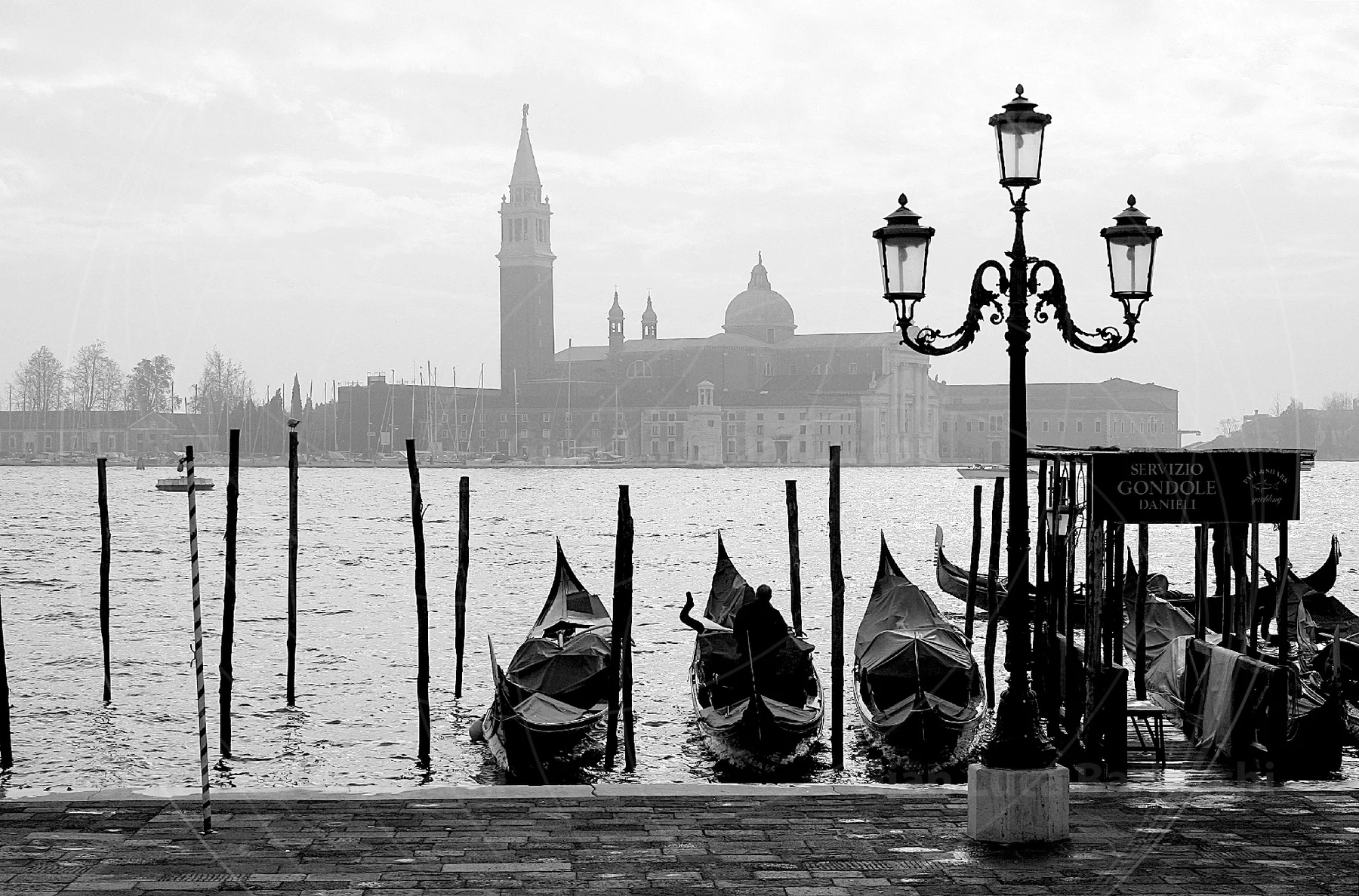 Black-and-white view of moored gondolas and a streetlamp beside the water in Venice