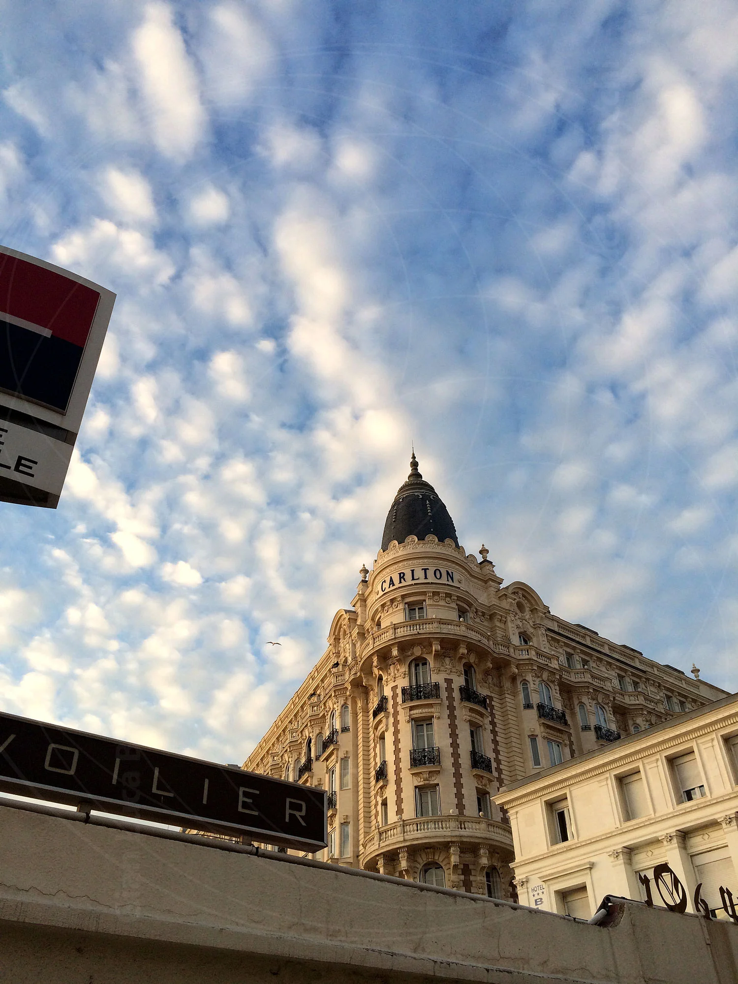 Ornate corner building beneath a cloud-filled blue sky in Cannes