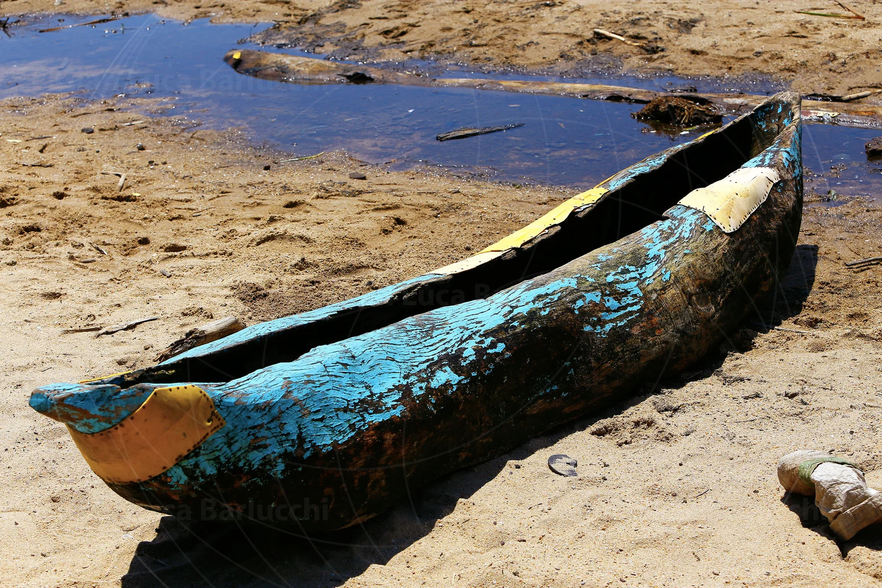 Blue-painted wooden canoe resting on a sandy shoreline