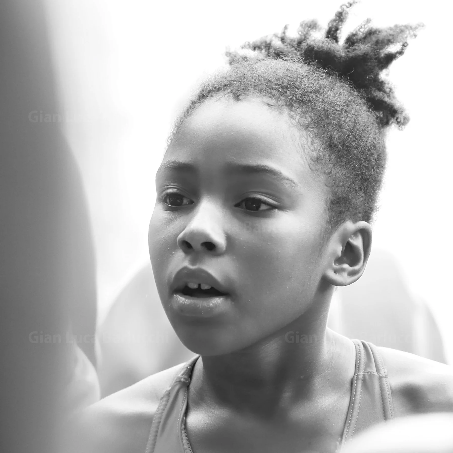Black-and-white portrait of a child with hair tied up, looking to the side