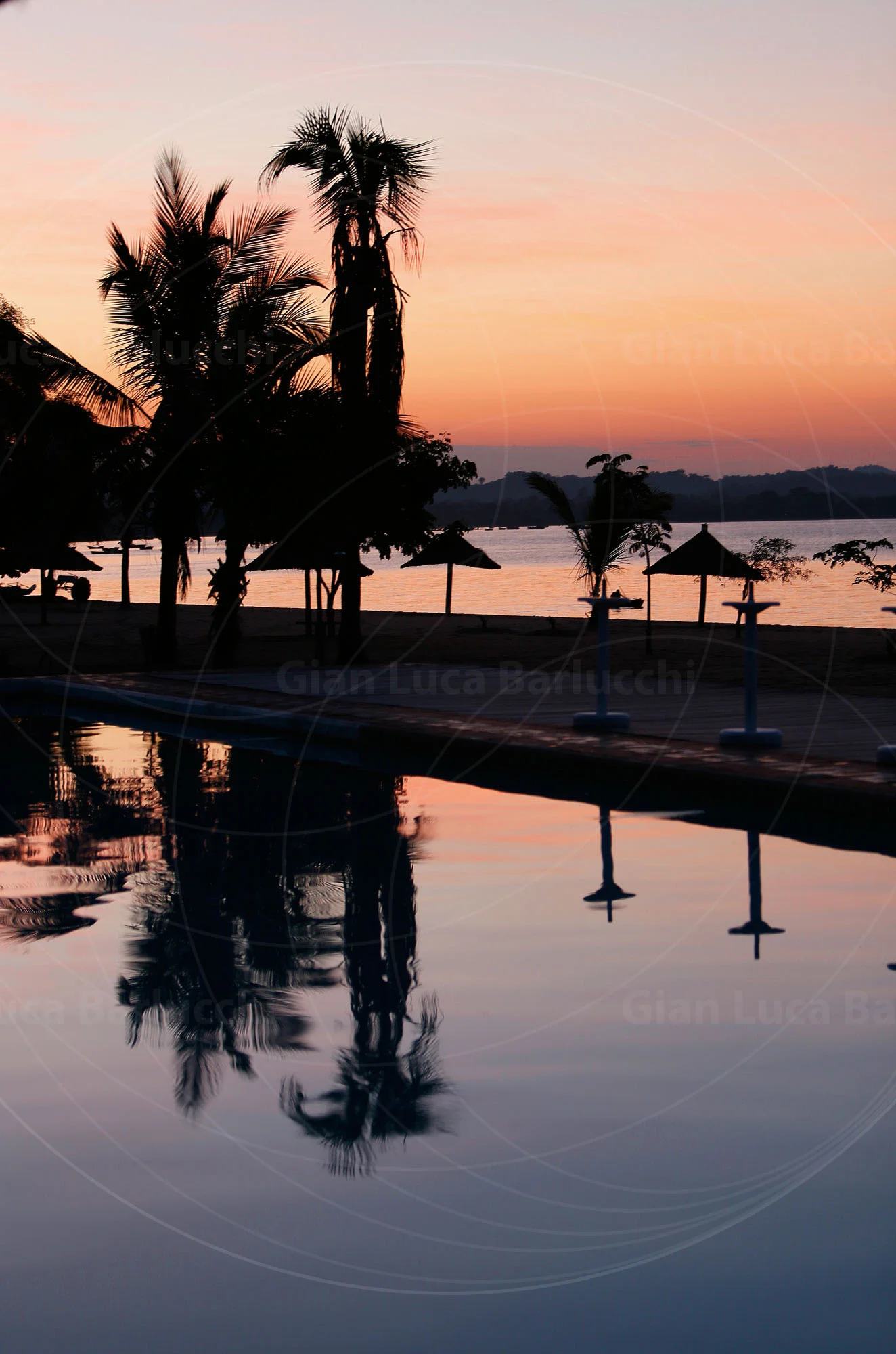 Palm trees and a sunset reflected in a swimming pool beside a lake