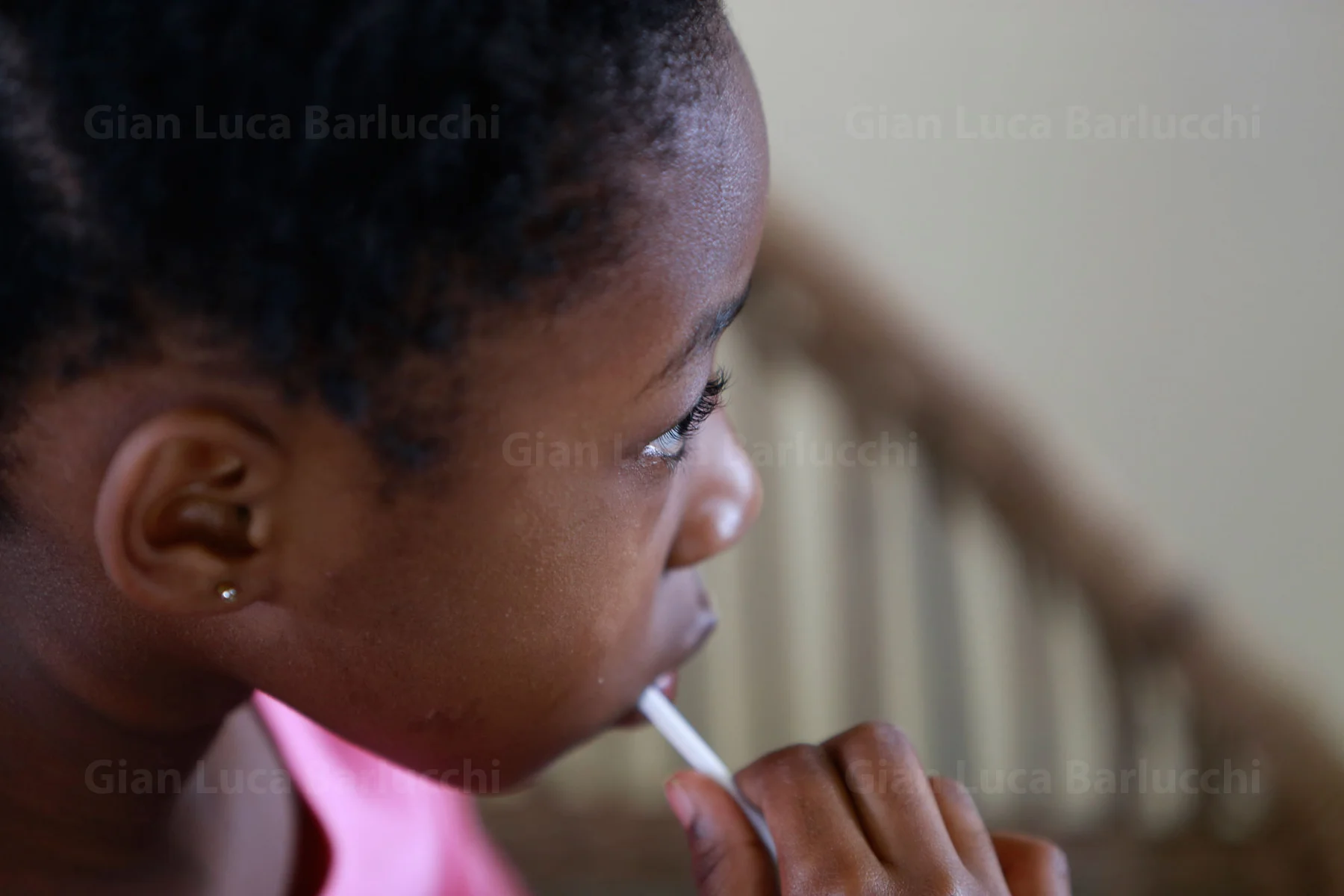 Side profile of a child in a pink top holding a lollipop