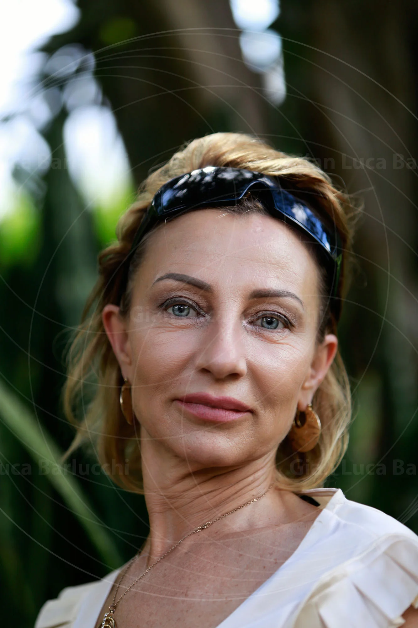 Woman with sunglasses resting on her head, framed by green foliage
