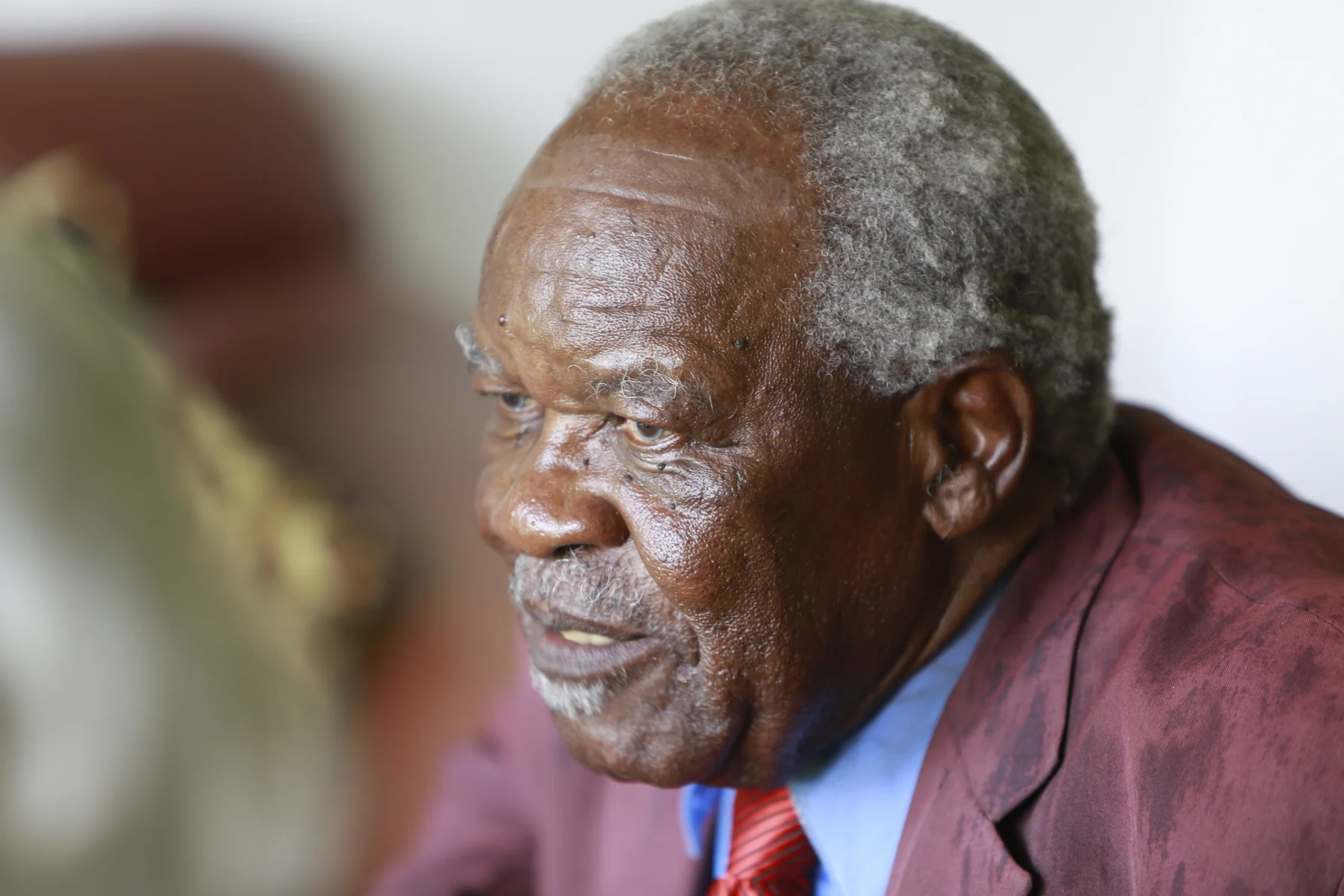 Close-up portrait of an older man in a burgundy jacket and striped tie