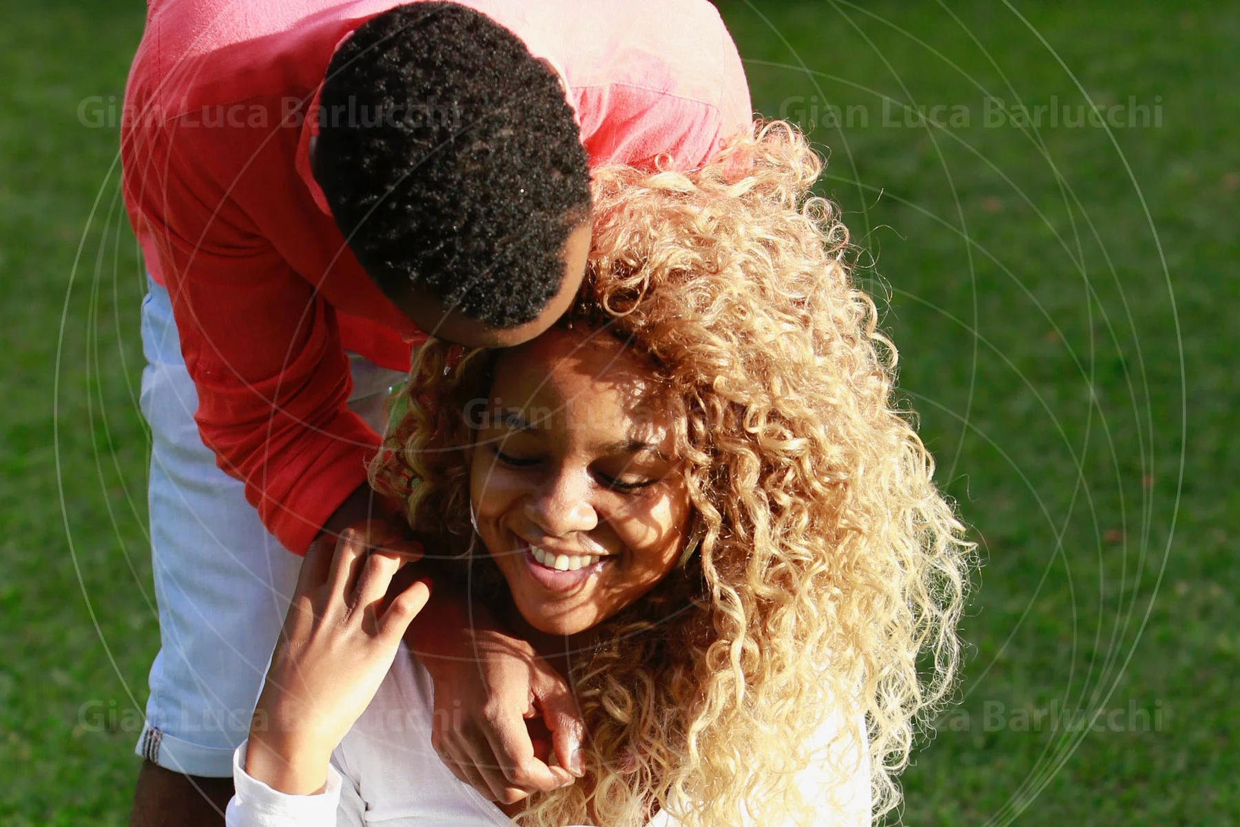 Man leaning over a smiling woman with curly hair outdoors