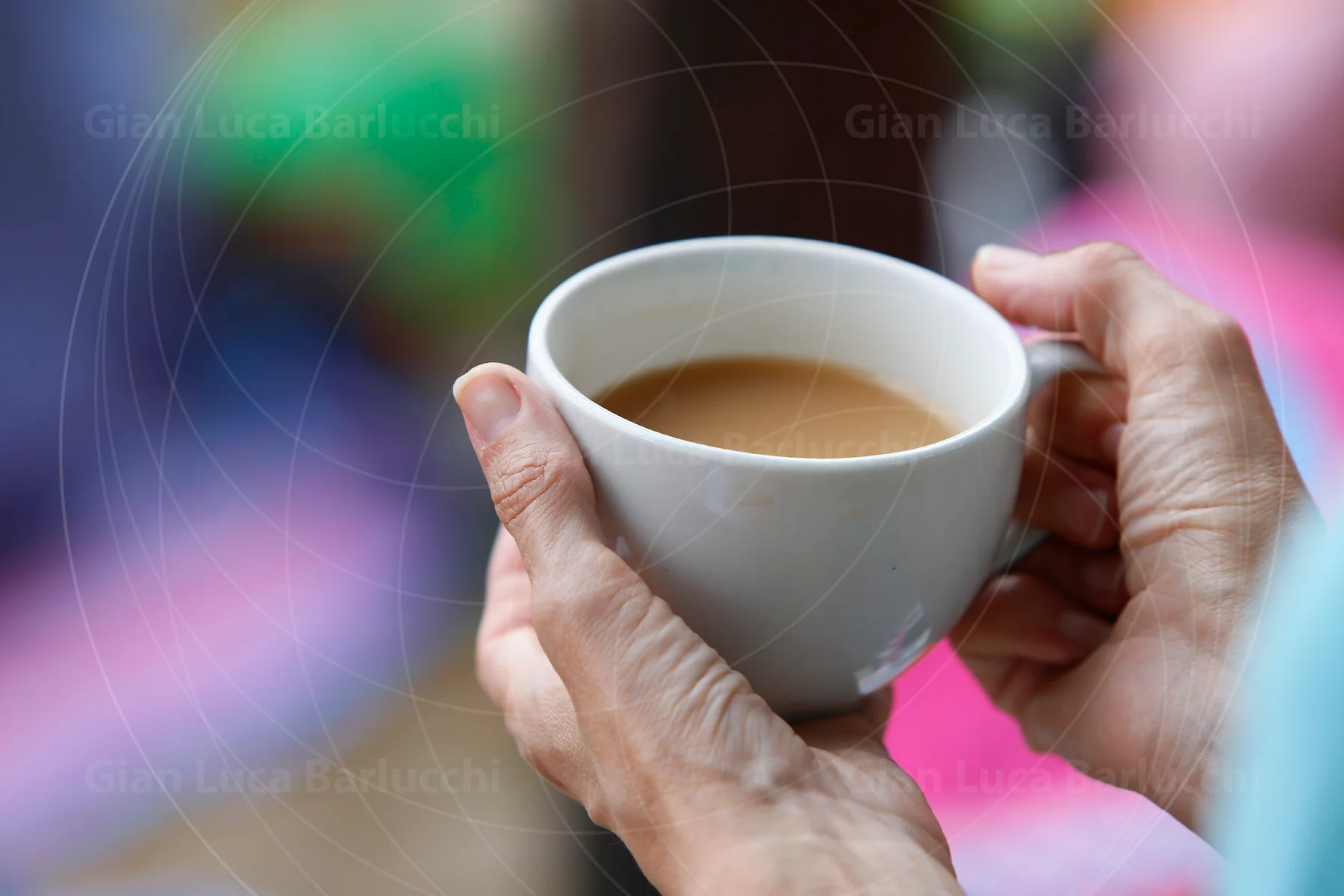 Hands wrapped around a white cup filled with a hot drink