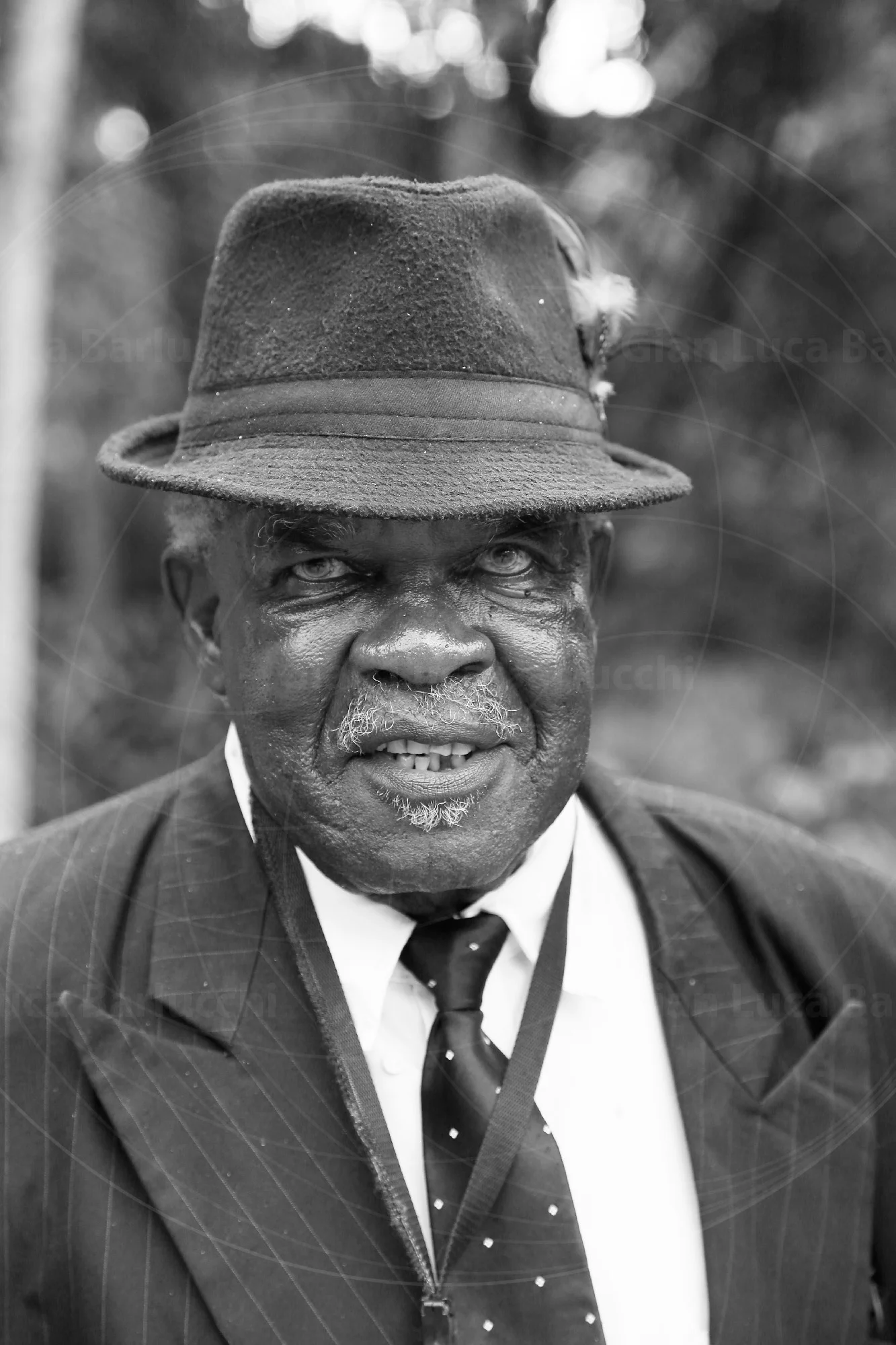 Black-and-white portrait of a smiling older man wearing a hat and tie