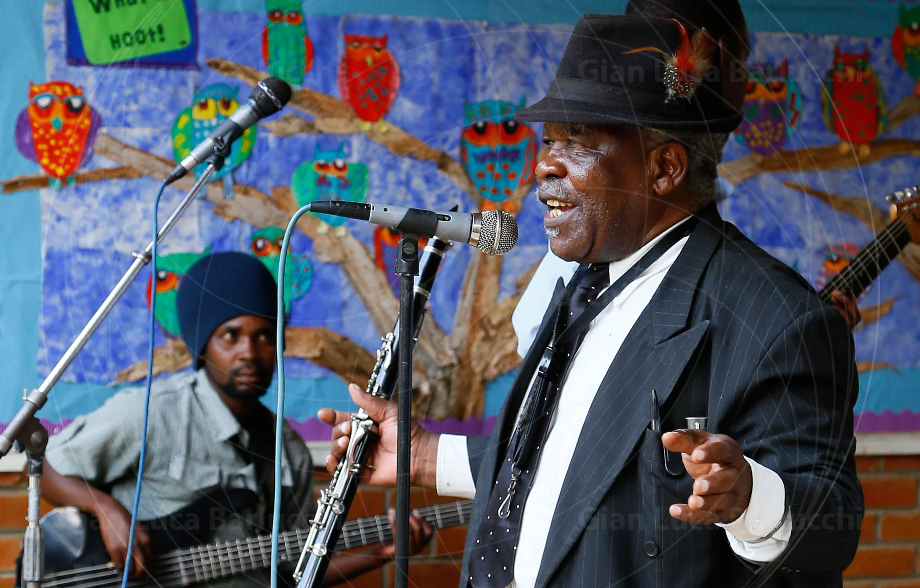 Musician singing into a microphone while holding a saxophone on stage